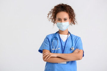 Female African-American doctor wearing medical mask on light background