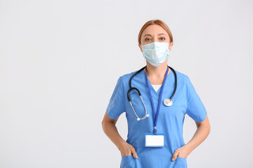 Fototapeta na wymiar Portrait of female doctor wearing medical mask on light background
