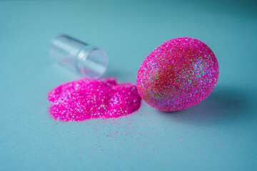 Trendy Easter background with shiny pink colored egg on a blue light background with empty bottle of glitter powder. Easter concept. Creative spring holiday image with painted chicken egg