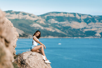Joyful woman travel mountains. Authentic blond female relax in picturesque landscape. A girl with developing natural hair is wearing a white top and denim shorts.