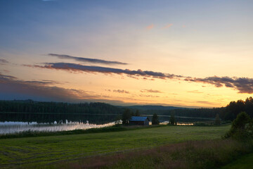 A lonely house by a lake in a wooden landscape in sunset.