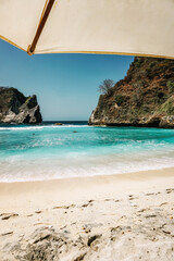 Beautiful sandy beach with an umbrella. Chilling in the sun and enjoying the blue ocean of Bali, Indonesia.