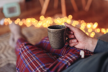 Man in check pyjamas sitting on a couch with a cup of tea