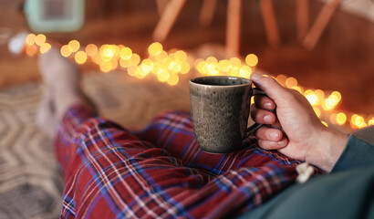 Man in check pyjamas sitting on a couch with a cup of tea