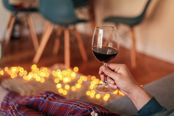 Man in check pyjamas holding a glass of red wine, cosy living room with candid light