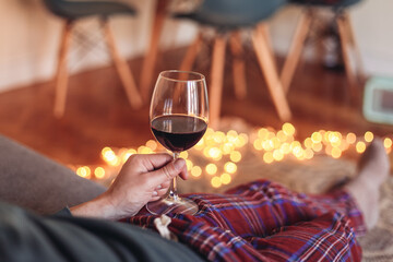 Man in check pyjamas holding a glass of red wine, cosy living room with candid light