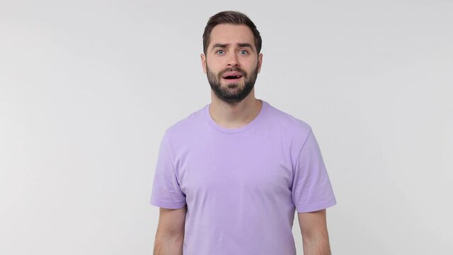 Joyful bearded young man 20s years old in violet t-shirt isolated on white background studio. People lifestyle concept. Pointing finger camera on you waving and greeting with hand as notices someone