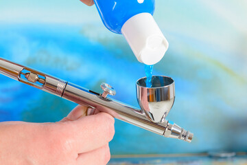 Artist fills the airbrush canister with blue paint
