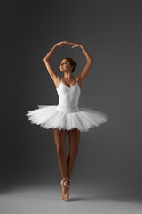 beautiful ballerina in white tutu and pointe shoes dancing on gray background © Rychko Yevhen