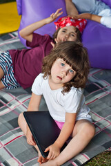 Children play in nature with a laptop. Boys and girls are resting in a tent camp. Children sit on the carpet on the grass in summer.