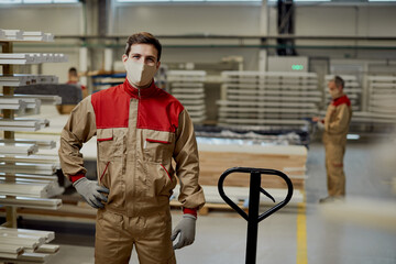 Happy carpenter with protective face mask standing at workshop and looking at camera.