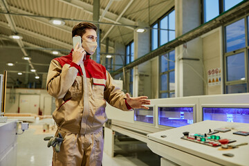Factory worker talking on the phone while supervising automated woodworking machine during...
