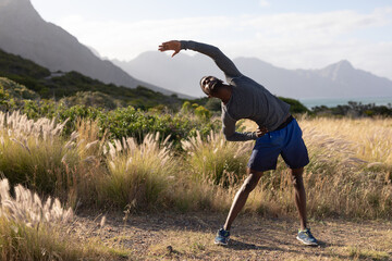 Fit african american man in sportswear stretching in tall grass