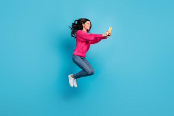 Fototapeta na wymiar Full size profile side photo of pretty girl hold look phone jump air wear pink sweater jeans isolated on blue color background