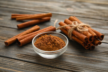 Cinnamon sticks and bowl with powder on wooden background