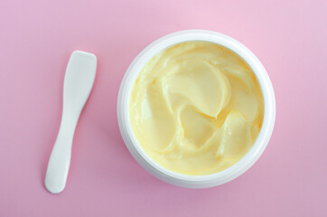 Yellow facial mask (banana face cream, shea butter hair mask, body butter). Natural skin and hair concept. Pink background. Top view, copy space.