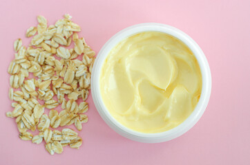 Yellow facial cream (hair mask, body butter) in a small white container and oatmeal. Natural skin and hair concept. Top view, copy space.