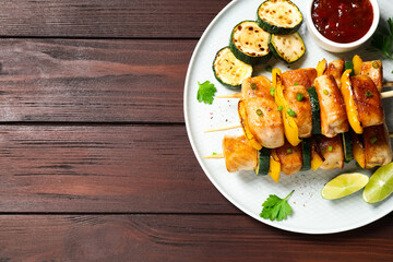 Fototapeta na wymiar Delicious chicken shish kebabs with vegetables and sauce on wooden table, top view. Space for text