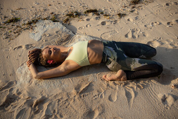 Yoga on the beach. Beautiful woman lying on the sand, practicing Supta Virasana, Reclining Hero Pose. Slim body. Healthy spine. Yoga retreat in Bali. Indonesia