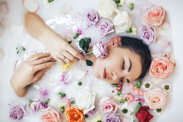 Obraz na płótnie Canvas The woman takes a wellness bath filled with milk. The buds of multi-colored roses float on the surface. Relaxing and anti-aging treatments