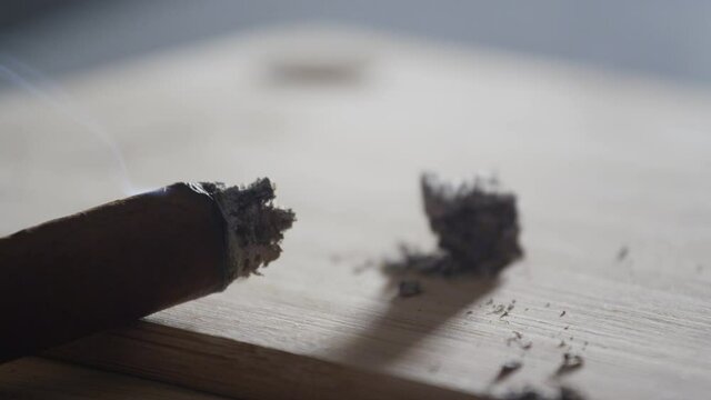 A burning cigar in a classic black ashtray streaming smoking in a dark, moody setting. Shot with a Nikon D7100 24MP camera at f7, 30 shutter speed.