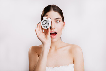 Close-up portrait of beautiful lady with white alarm clock covering her eyes. No makeup