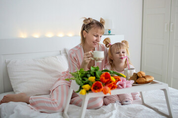 mom and daughter have breakfast in bed in pajamas