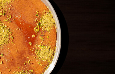 Traditional eastern dessert kunafa in a big aluminium dish on dark black background with copy space. Top view. Arabic cheese kunafa on dark. Konafa.