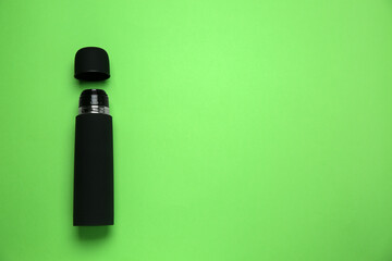 Black thermos and cup on green background, flat lay. Space for text