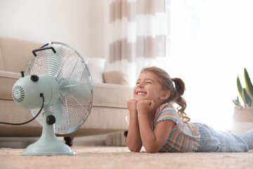 Little girl enjoying air flow from fan on floor in living room. Summer heat