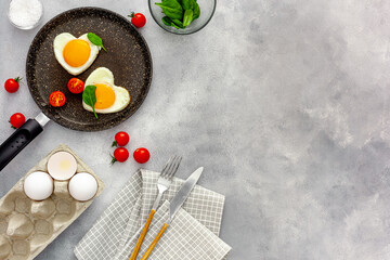 Cooking heart-shaped fried eggs in a pan with tomatoes and greens