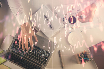 Multi exposure of man's hands typing over computer keyboard and forex graph hologram drawing. Top view. Financial markets concept.