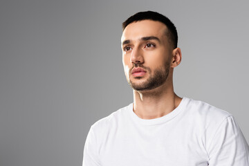 confident, brunette hispanic man in white t-shirt looking away isolated on grey