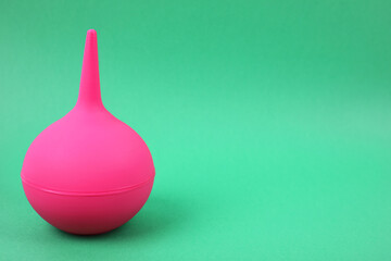 Pink enema on green background, space for text. Medical treatment