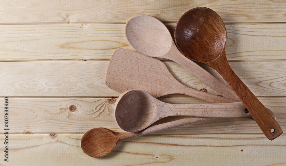 Wall mural New spoons, ladles and spatula kitchen utensil set on wooden plank table, boards background and texture, top view 