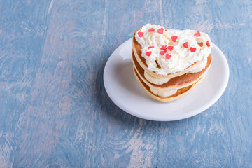 Romantic breakfast in bed. Homemade pancake in the shape of a heart. Pancakes laid out in a stack with banana and decorated with white cream with red hearts on a white plate