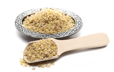 Dry bulgur pile with wooden spoon and oriental engraved and decorated metal bowl isolated on white background