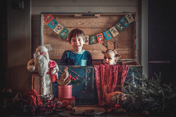 Cute little boy and his funny baby sister in deer antlers hat are playing in old vintage chest full of retro christmas stuff. Image with selective focus, noise effects and toning