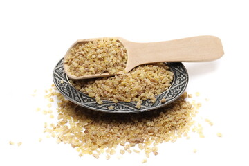 Dry bulgur pile with wooden spoon and oriental engraved and decorated metal bowl isolated on white background