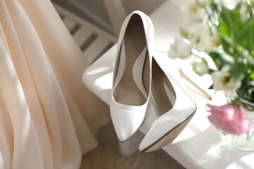 Pair of white high heel shoes, flowers and wedding dress indoors