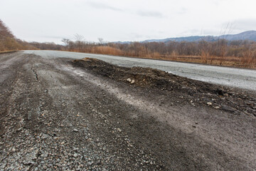 Bad Russian asphalt road. The asphalt road is full of holes and cracks among dried autumn trees.