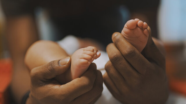 Black father playing with baby feet. Close up. High quality photo