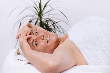 Satisfied and relaxed senior woman in a beauty salon wrapped in a white towel against a green...