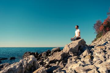 Attractive young man practicing yoga meditation and breathwork outdoors by the sea