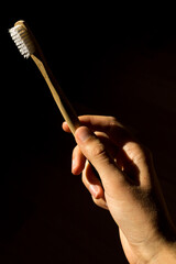 Hand holding an ecological zero waste toothbrush made of bamboo, isolated on dark background. 