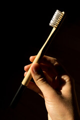 Hand holding an ecological zero waste toothbrush made of bamboo, isolated on dark background. 