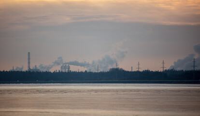 Fototapeta premium Smoke from chimneys of a metallurgical plant near a frozen lake