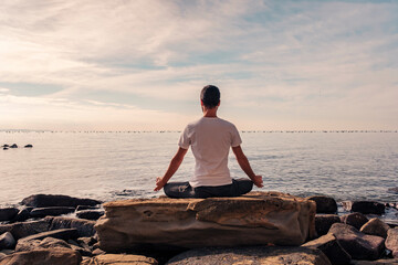 Attractive young man practicing yoga meditation and breathwork outdoors by the sea