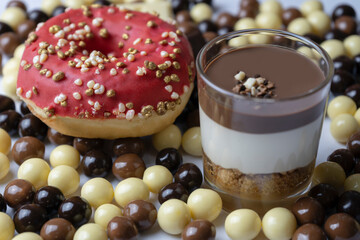 Closeup view of Chocolate dessert in glass (yogurt or cream, cookies and nuts )with red donut and chocolate balls (black chocolate, milk chocolate and white chocolate ).