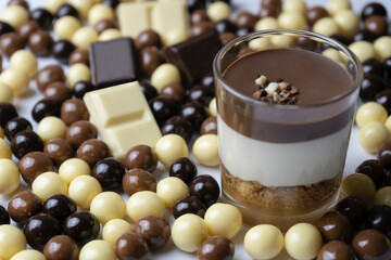 Chocolate dessert in glass (yogurt or cream, cookies and nuts )with chocolate balls (black chocolate, milk chocolate and white chocolate ).Tasty sweet concept background.